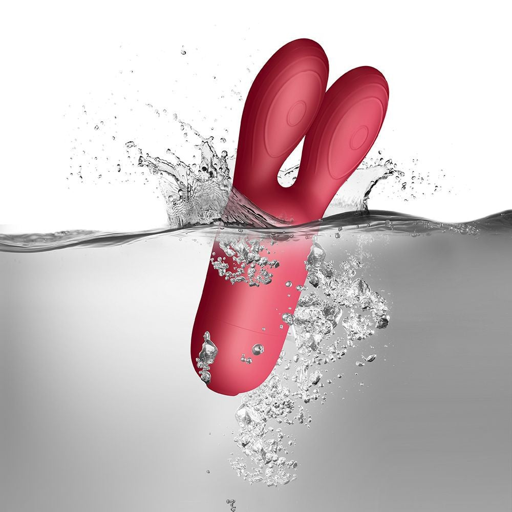 Red sex toy partially submerged in water with splashes on a gray background