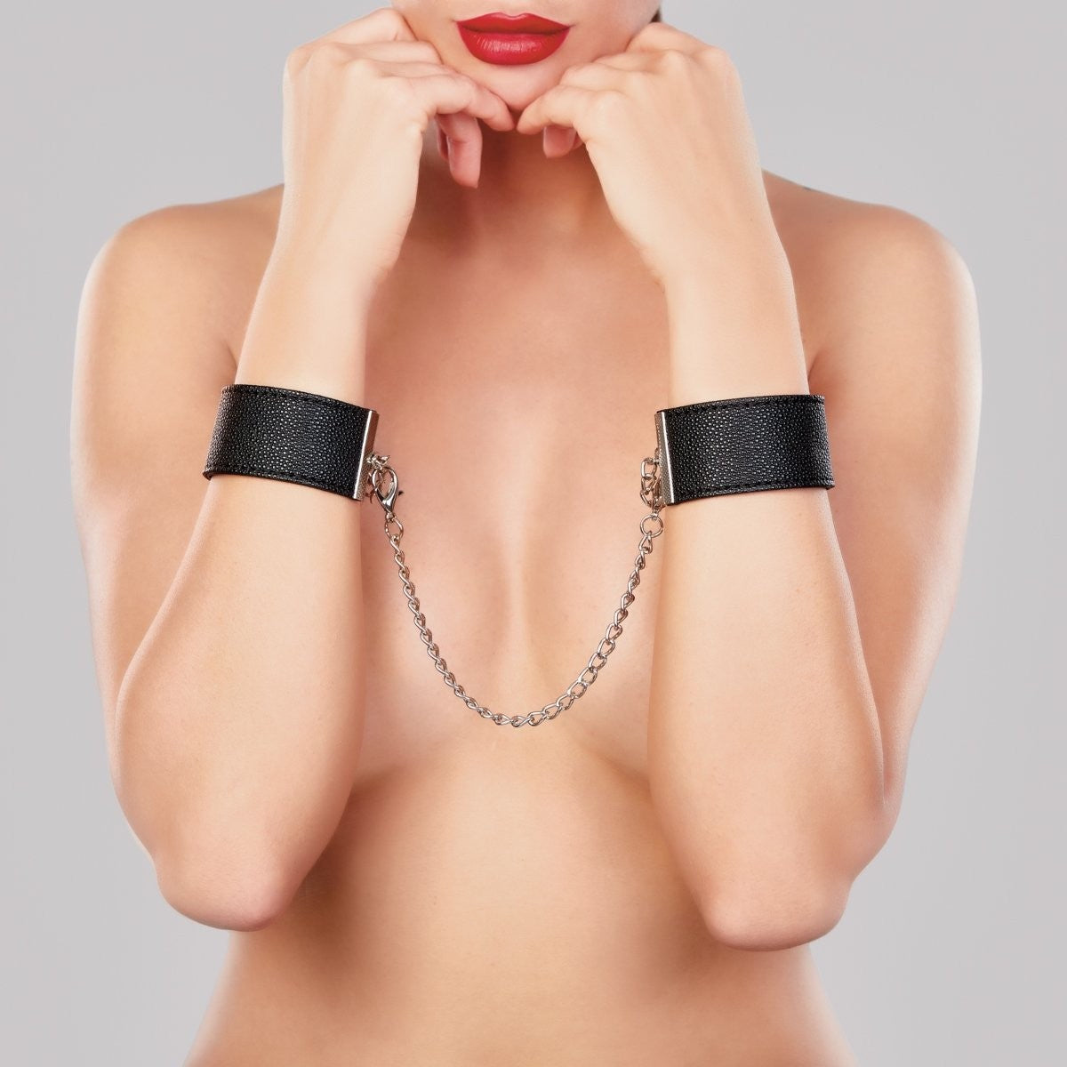 Person wearing black leather cuffs with a chain on a gray background