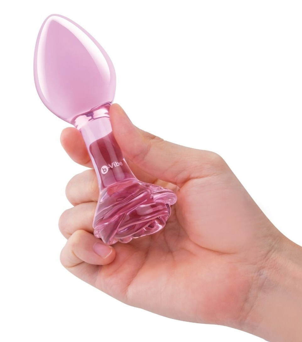 Pink glass sex toy held in a hand against a white background