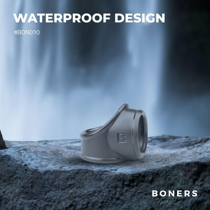 Gray cock ring on a rock with a waterfall in the background, featuring the brand 'BONERS'.
