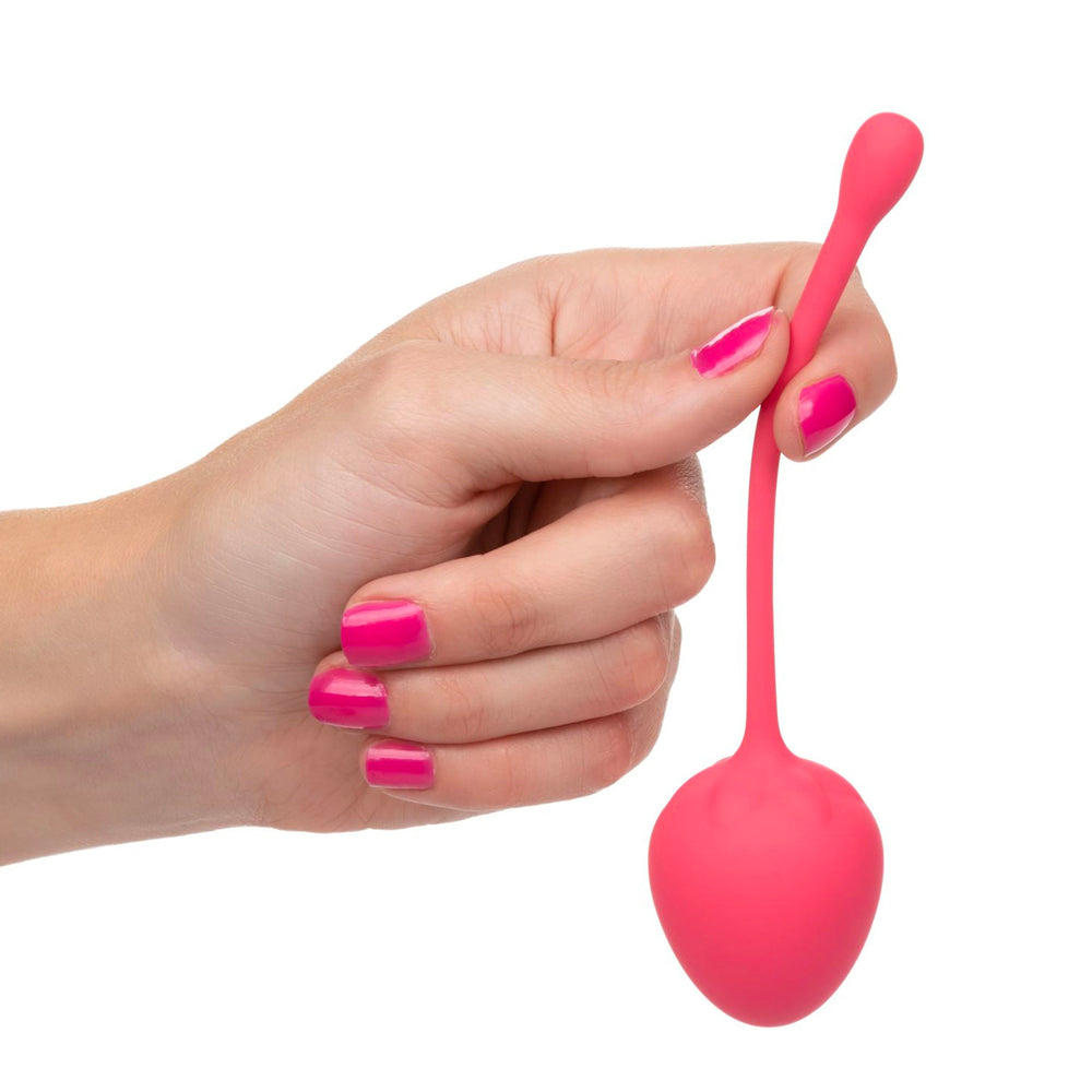 Hand holding a pink silicone kegel ball against a white background
