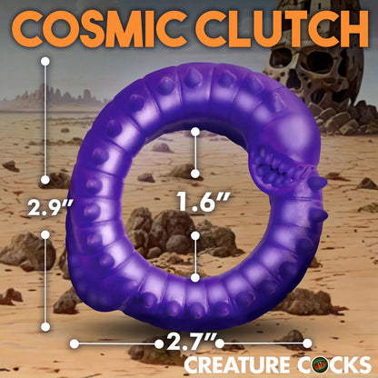 Purple penis ring with measurements against a desert landscape background, branded 'Cosmic Clutch' and 'Creature Cocks'.