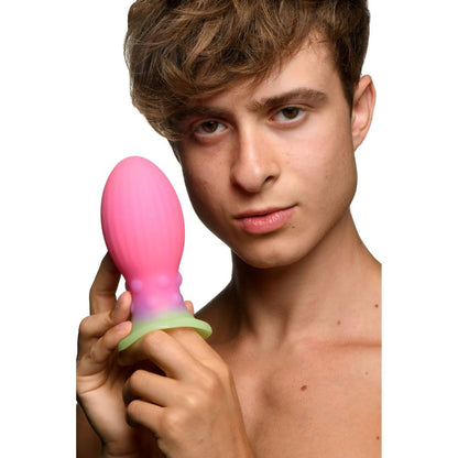 Person holding a pink and green anal toy against a white background