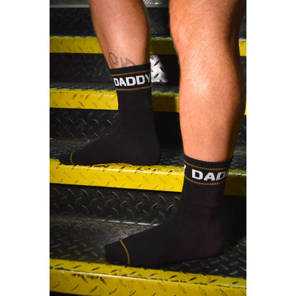 Black socks with 'DADDY' branding worn by a person on a textured surface.