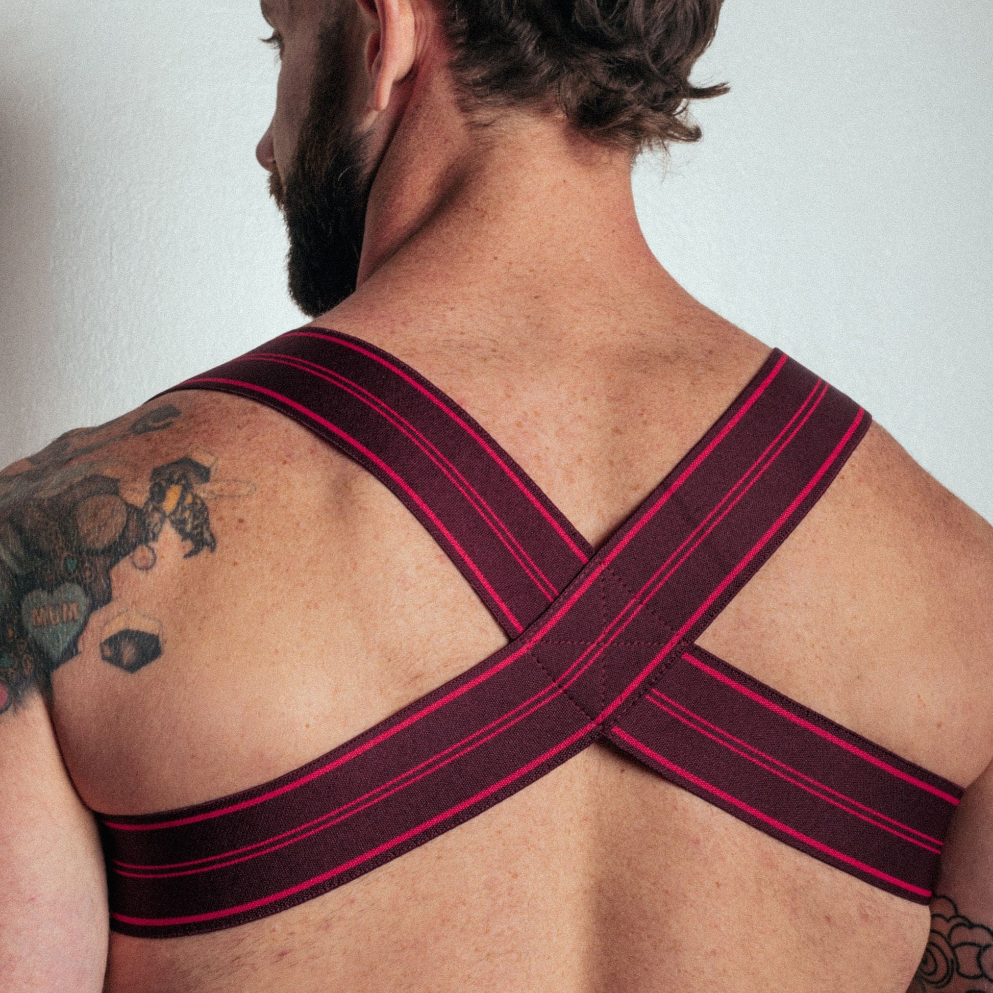 Man wearing a black and red strap across his back against a plain background