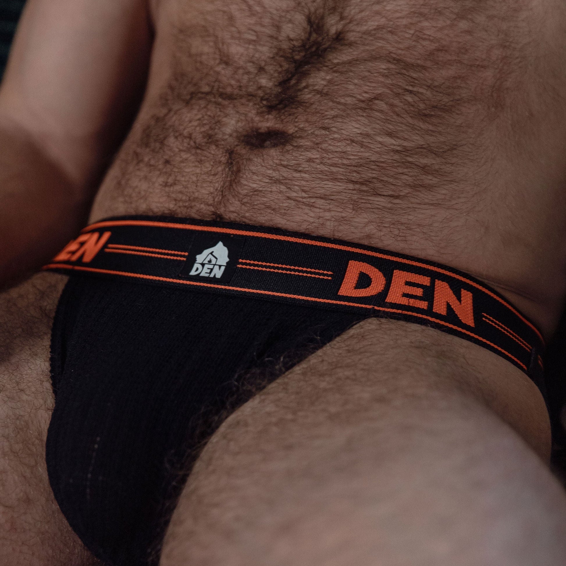 Black men's underwear with 'DEN' branding on a hairy chest.