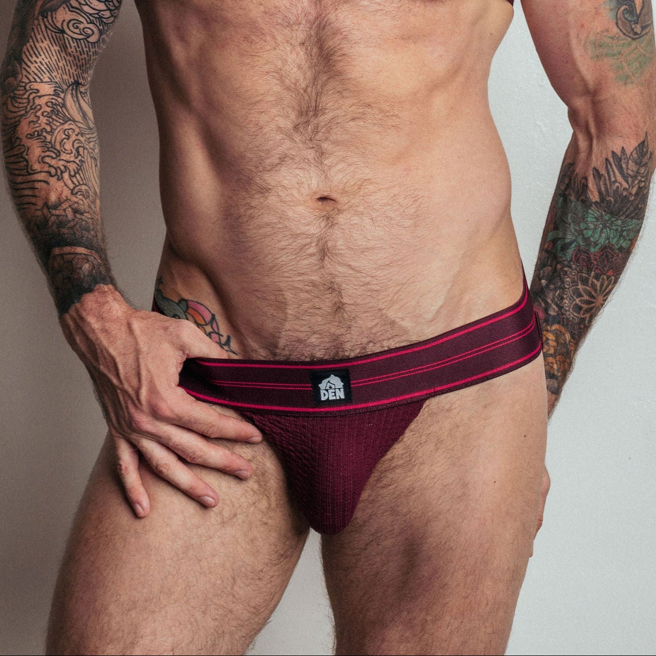 Man wearing a red Adidas sports bra and briefs against a plain background