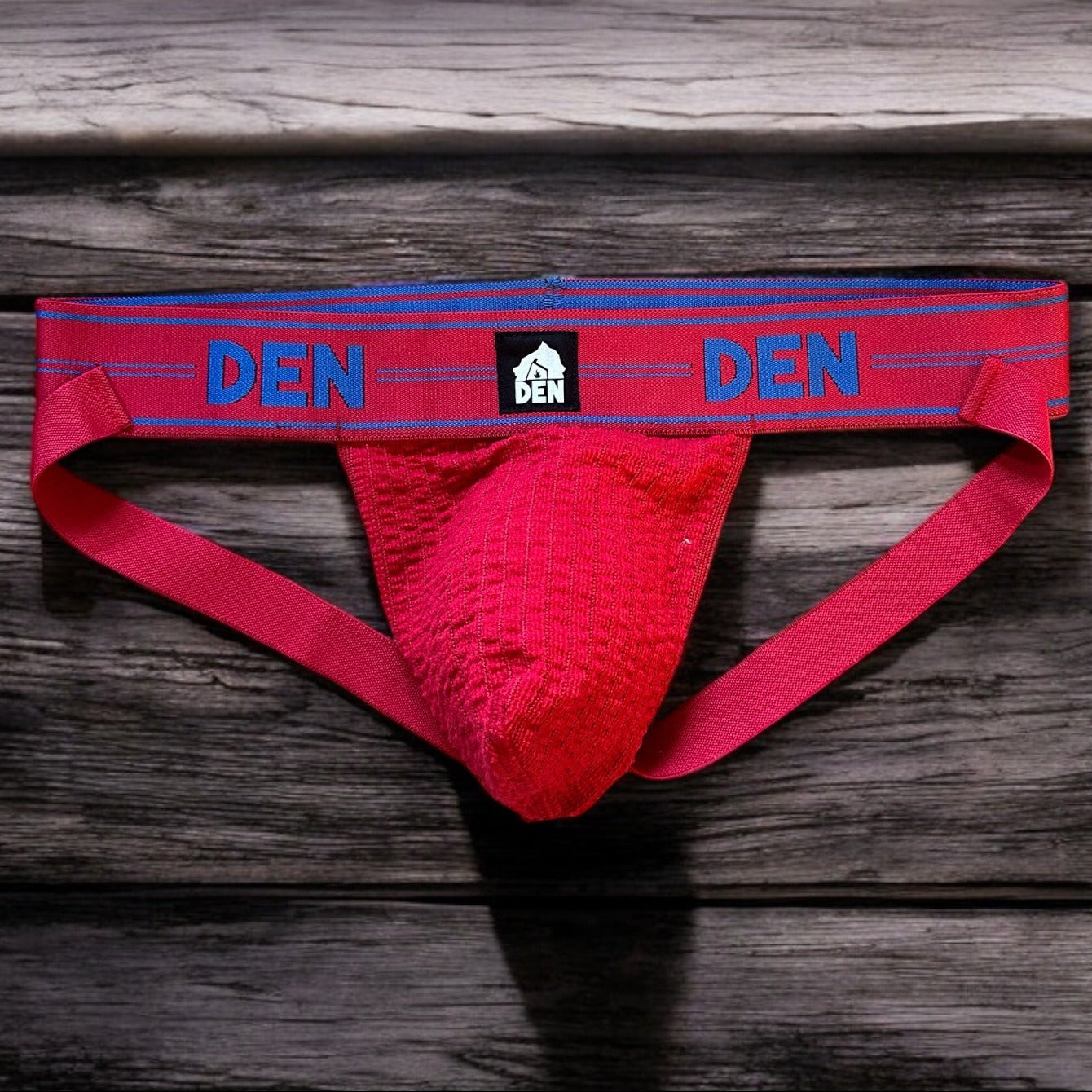 Red men's underwear with 'DEN' branding on a wooden surface