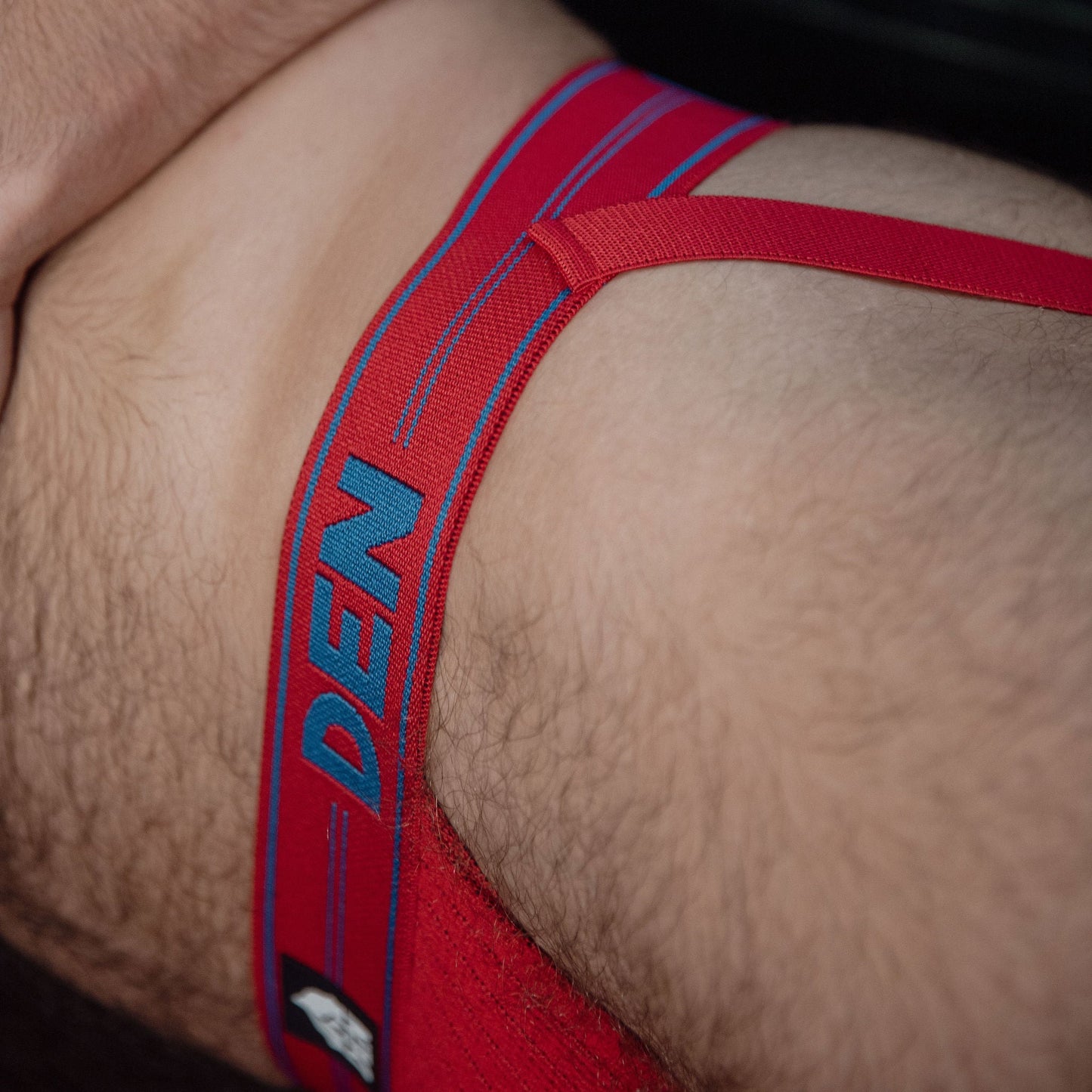 Red men's underwear with 'DEN' branding on a close-up of skin.