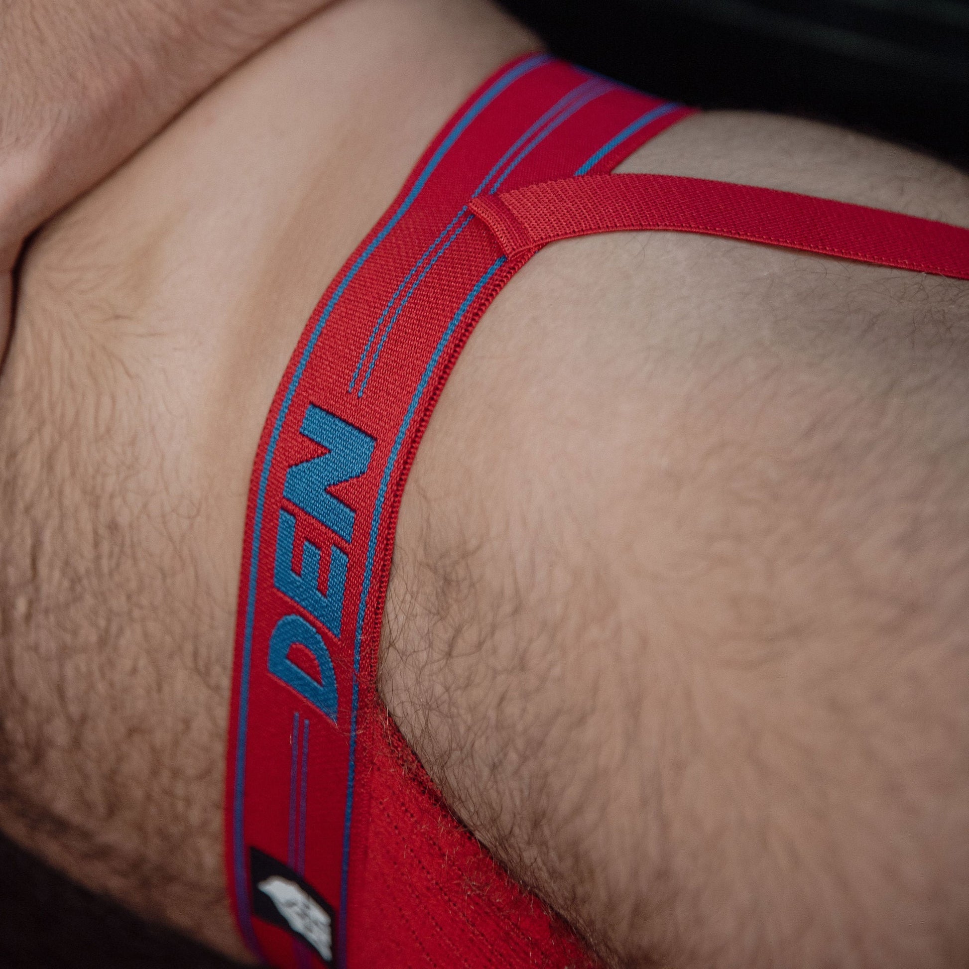 Red men's underwear with 'DEN' branding on a close-up of skin.