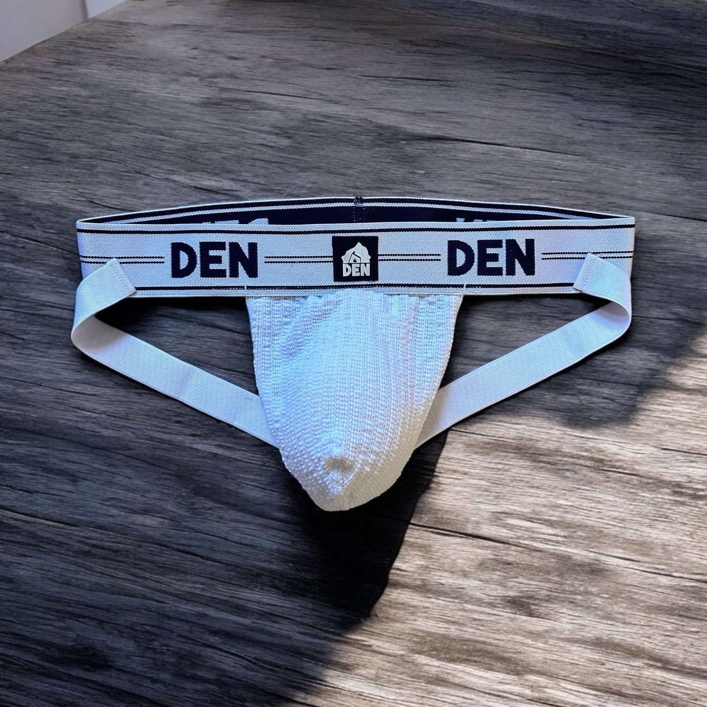 White men's underwear with 'DEN' branding on a wooden surface