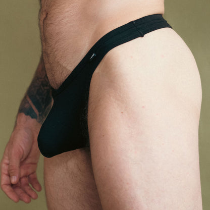 Man wearing a black thong against a green background