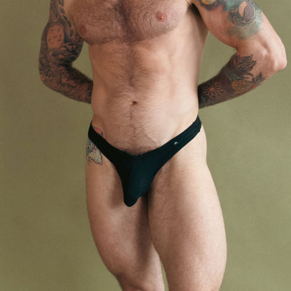 Man wearing a black thong against a beige background