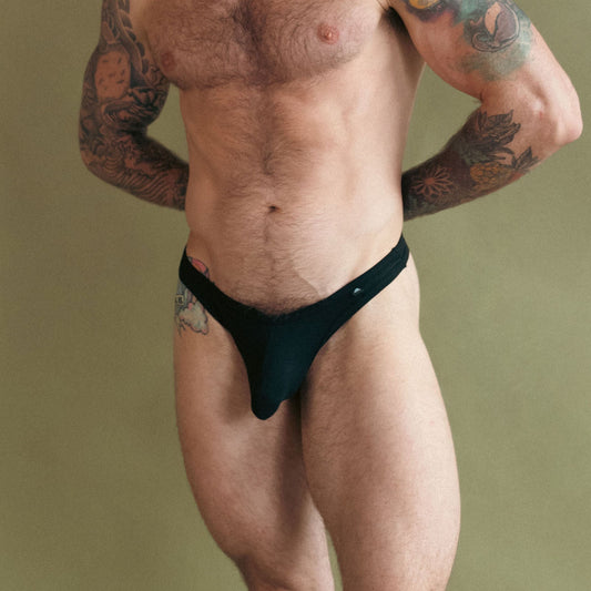 Man wearing a black thong against a beige background
