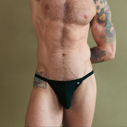 Man with tattoos wearing black underwear against a green background