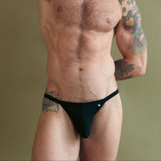 Man with tattoos wearing black underwear against a green background