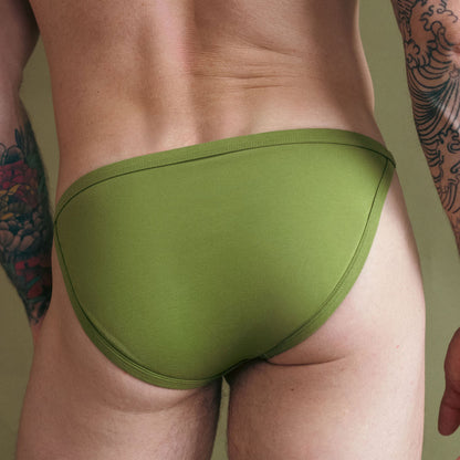 Green men's underwear on a person with tattoos against a neutral background