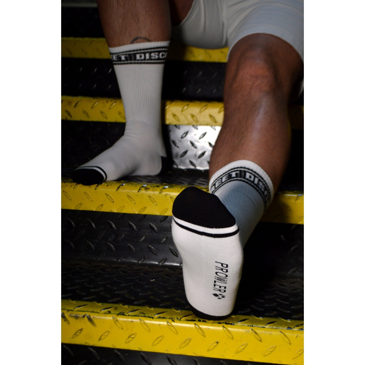 Person wearing white socks with black accents on a yellow and black textured surface