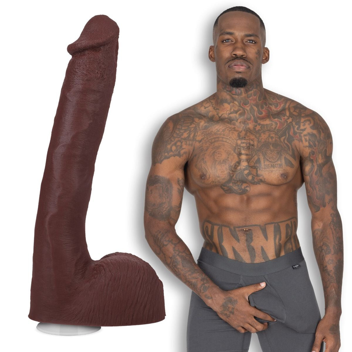 Man with tattoos wearing gray pants next to a large brown penis dildo on a white background