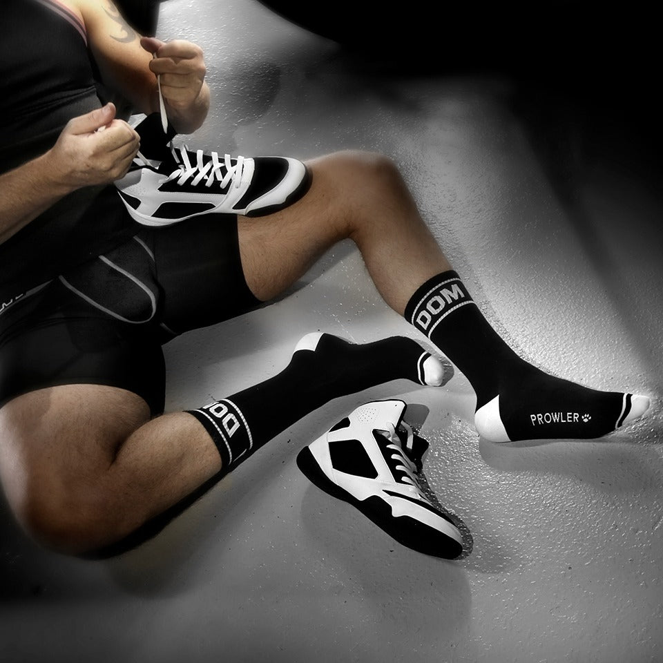 Person wearing black and white athletic shoes and socks with 'Prowler' branding on a gray surface.