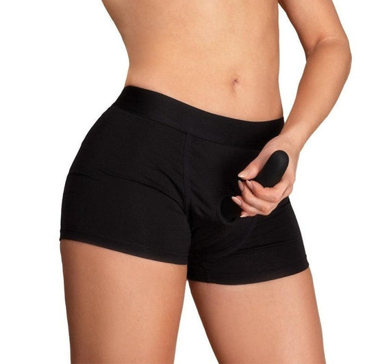 Person wearing black athletic shorts with attached strap-on dildo on a plain background