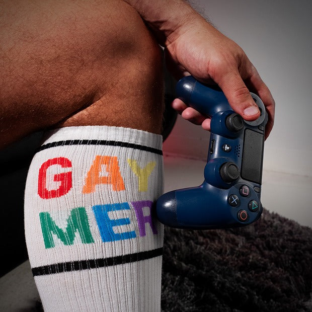 Person wearing a sock with 'GAY MER' in colorful letters, holding a gaming controller.