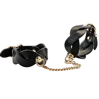 Black leather cuffs with gold chain links on a white background