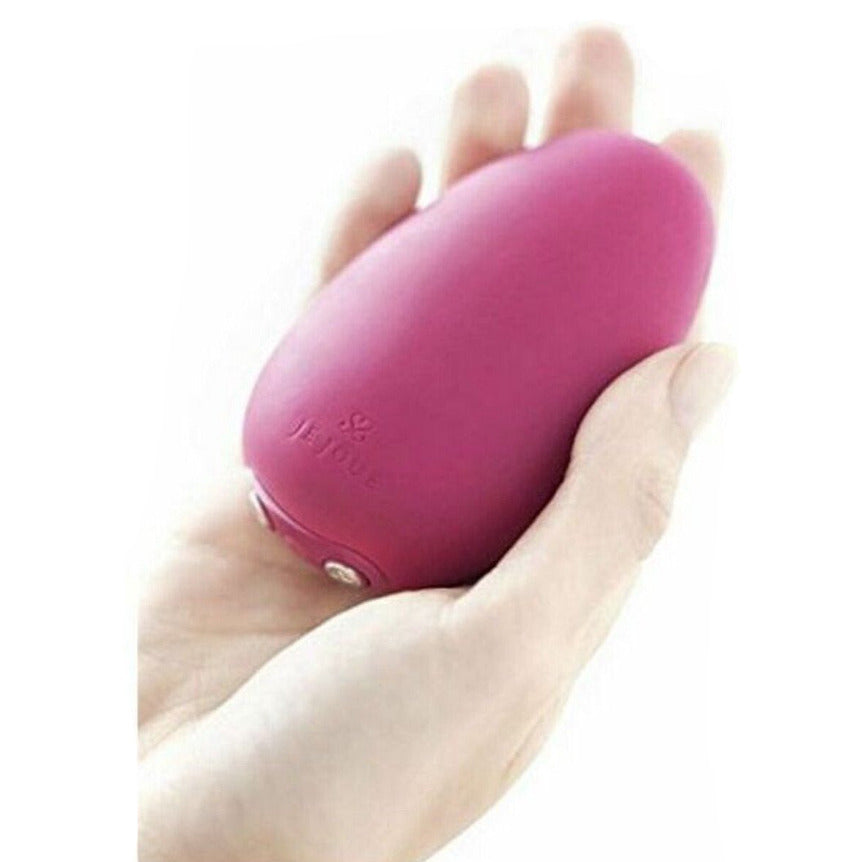 Pink handheld massager held in a hand against a white background