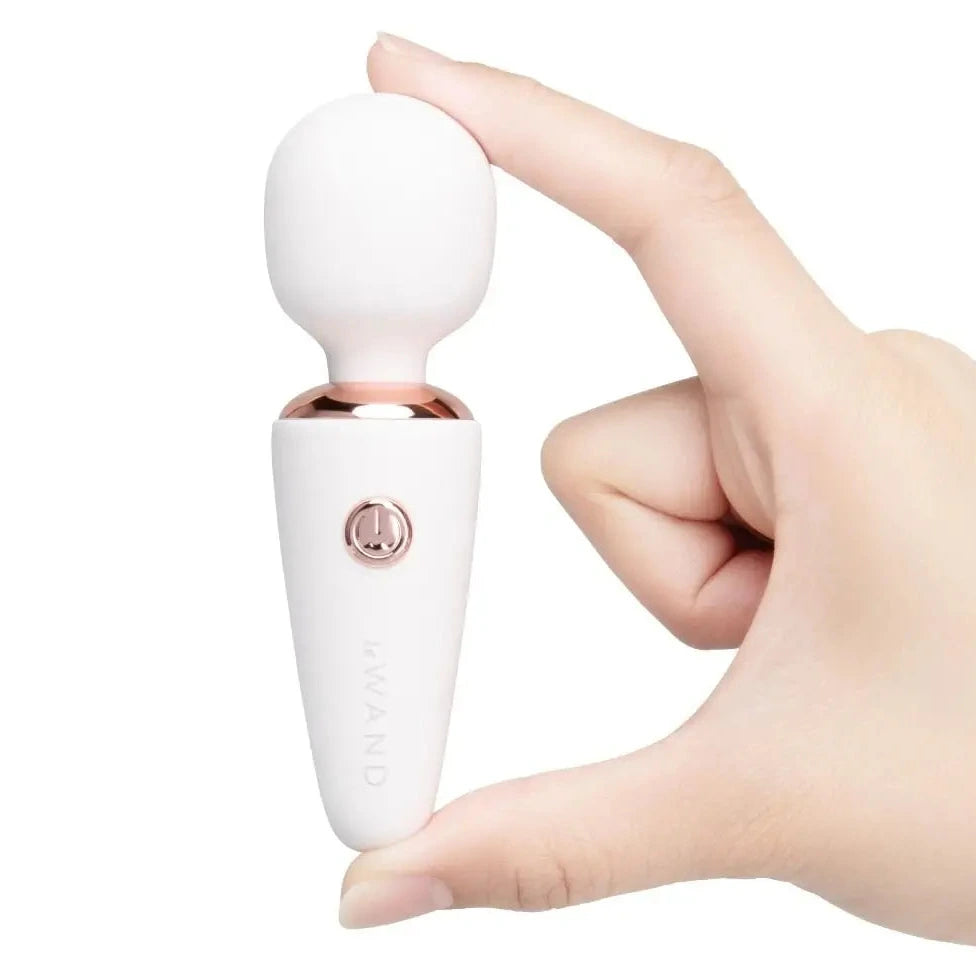 Hand holding a white and rose gold massager device on a white background