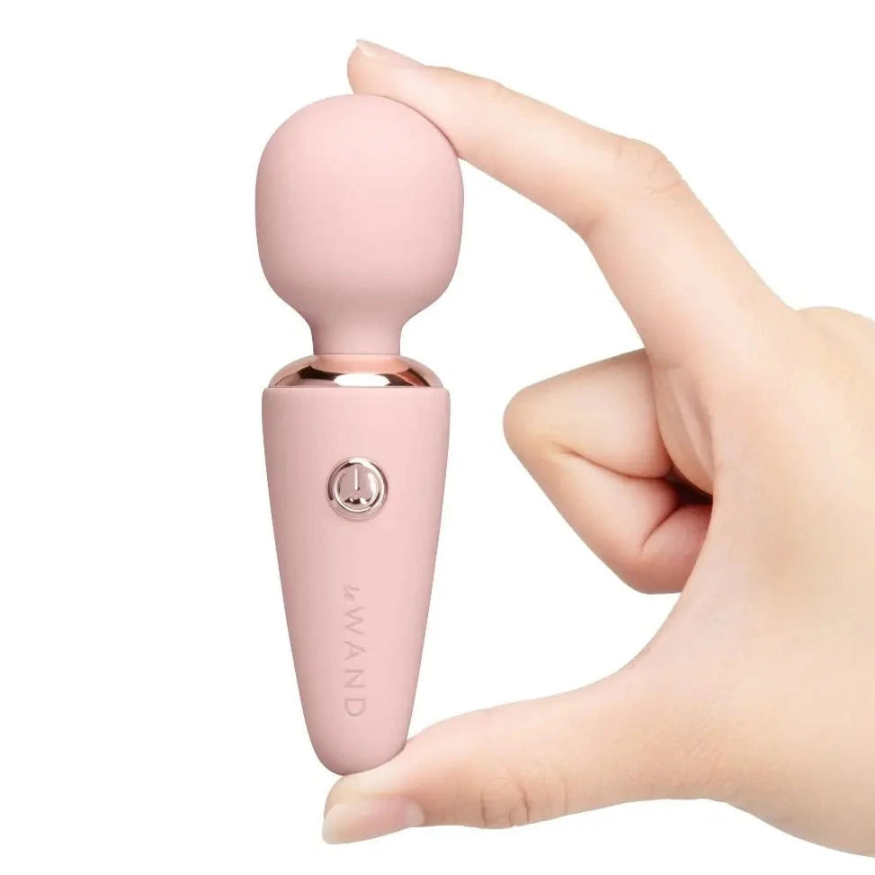 Pink handheld massager device held by a hand on a white background