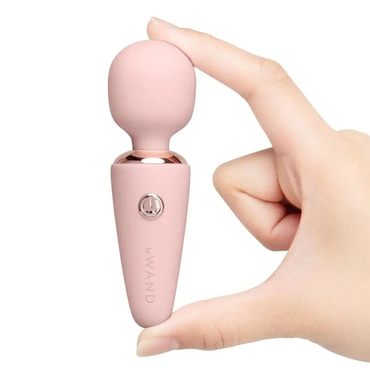Pink handheld massager device held by a hand on a white background