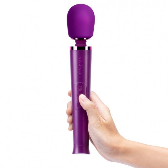 Purple handheld massager held in a hand against a white background