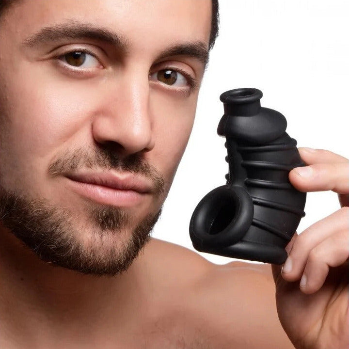 Man holding a black silicone chastity device close to his face on a white background