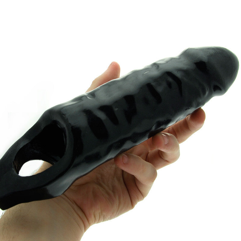 Black textured penis extender held in a hand against a white background