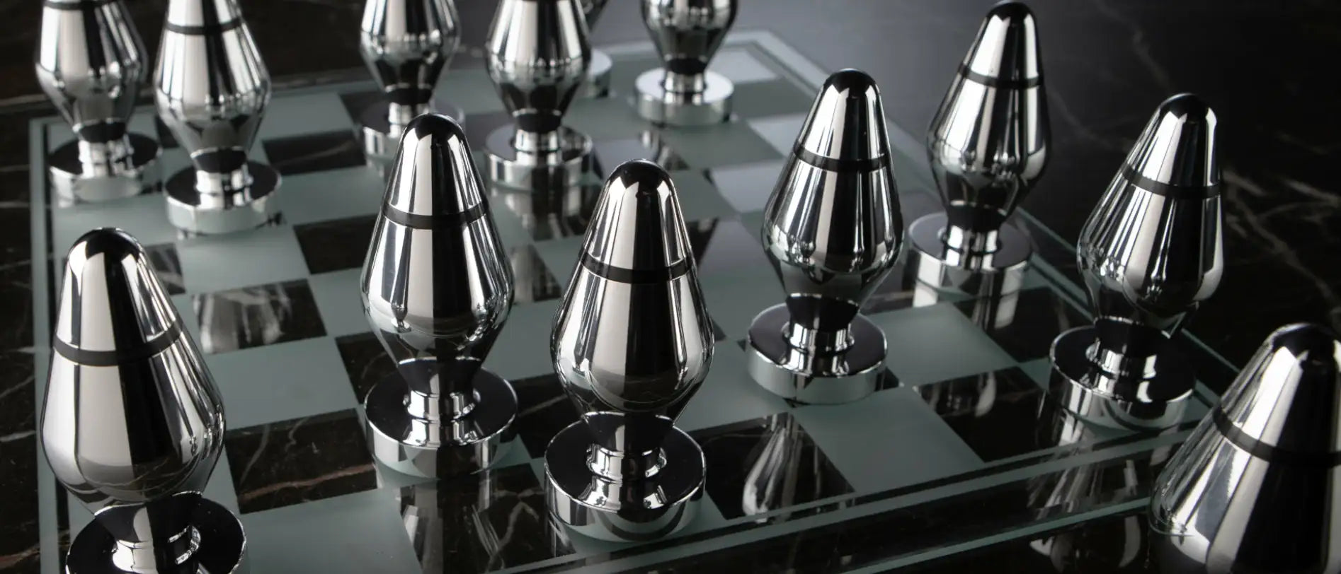 Metallic anal butt plugs as chess pieces on a reflective chessboard
