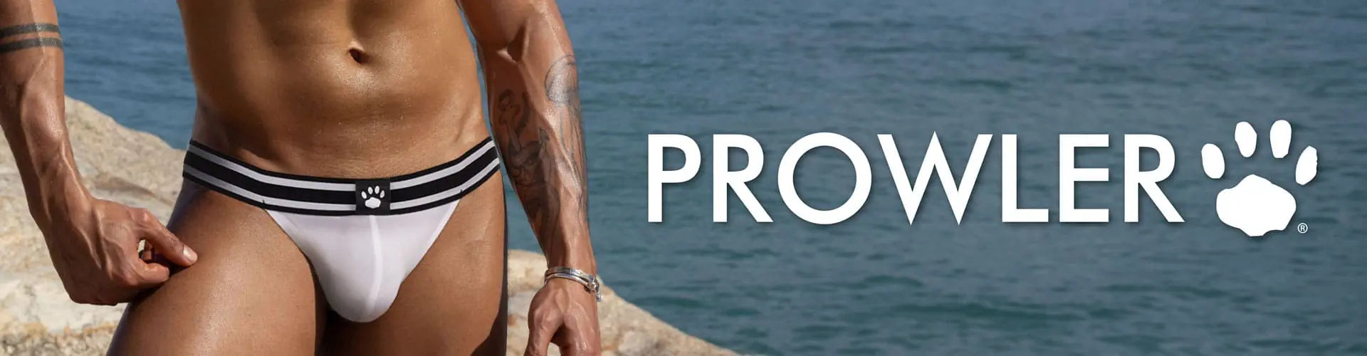 Man wearing white swimwear with black stripes on a rocky beach, Prowler brand logo visible.