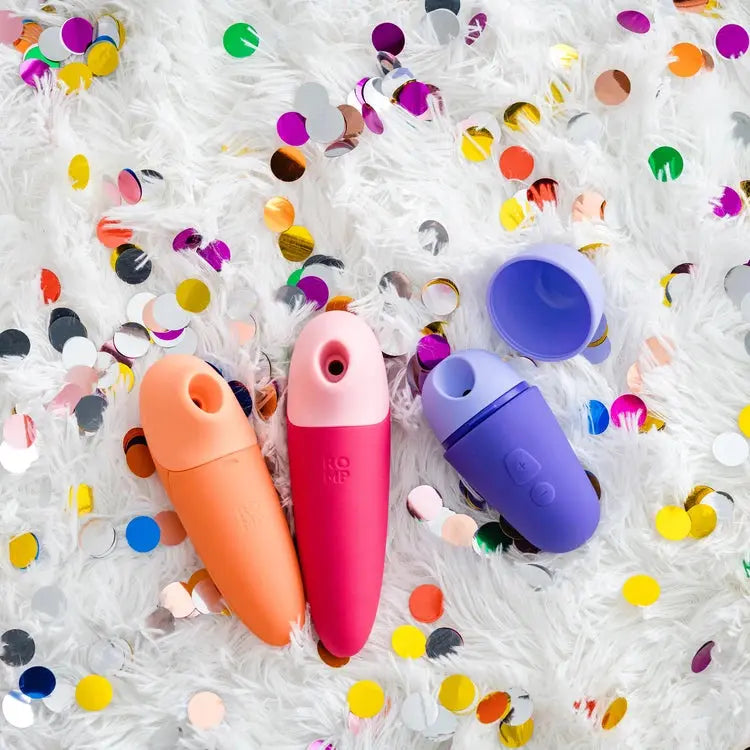Three colorful clitoral massagers on a white surface with confetti