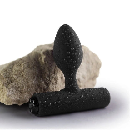Black anal massage tool with textured design on a rock and white background
