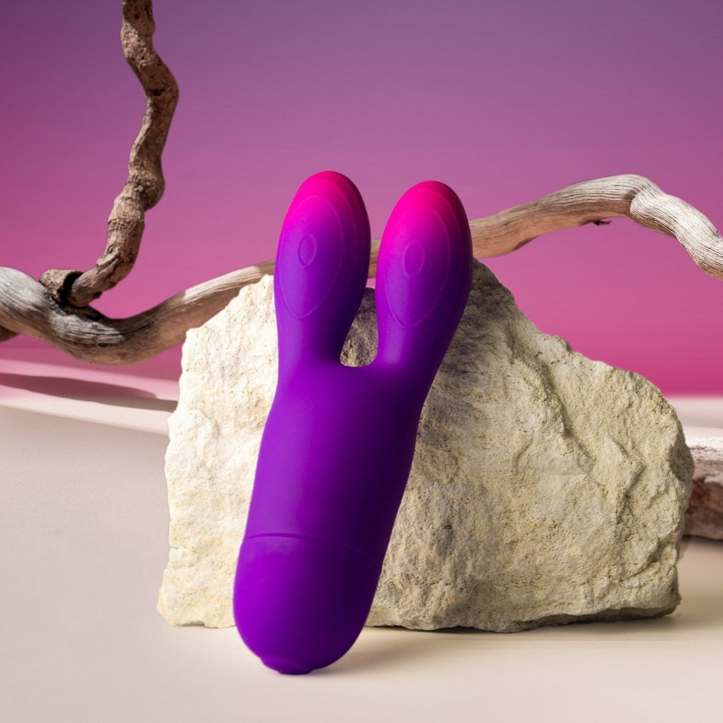 Purple and pink sex toy resembling a rabbit on a rock with a pink background