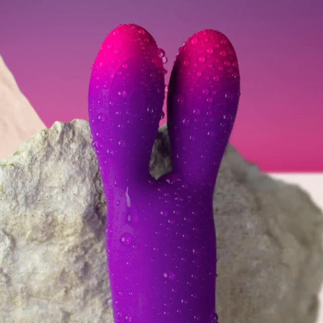 Purple massager resembling a rabbit against a rocky background with a pink sky.