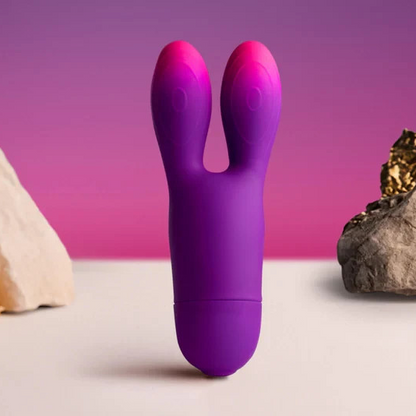 Purple and pink sex toy resembling a rabbit on a table with rocks and crystals.