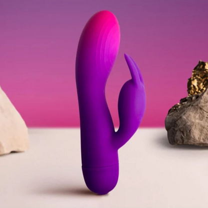 Purple silicone rabbit vibrator on a surface with rocks and a pink background