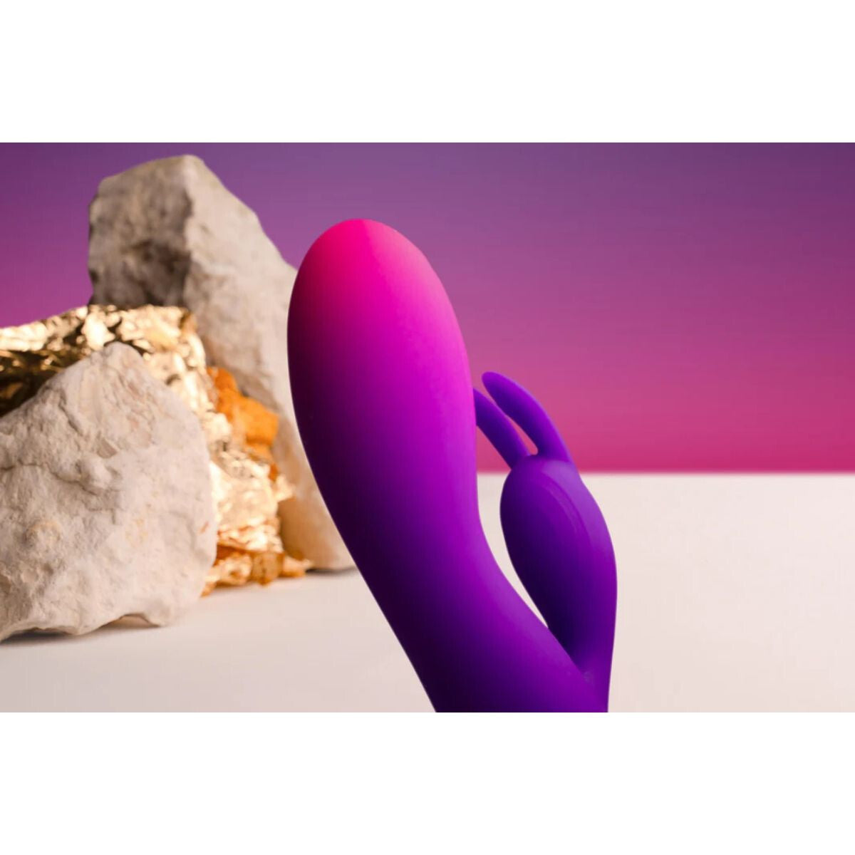 Purple and pink sex toy resembling a rabbit on a white surface with a purple background