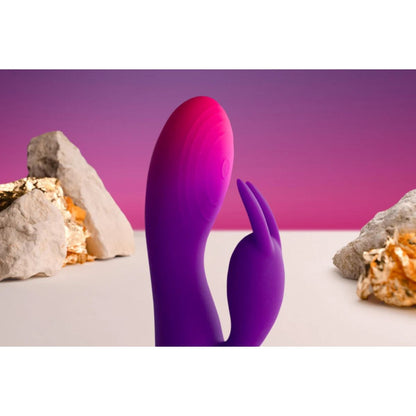 Purple silicone vibrator with natural rock formations on a white surface and purple background