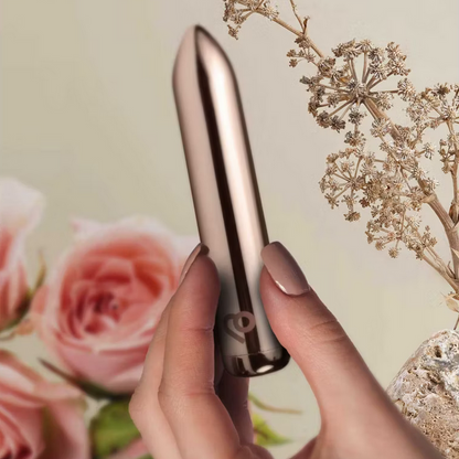 Hand holding a metallic device with flowers and branches in the background