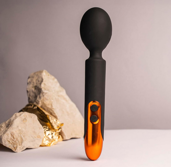 Black and orange handheld massager with a rock and gold nugget on a neutral background