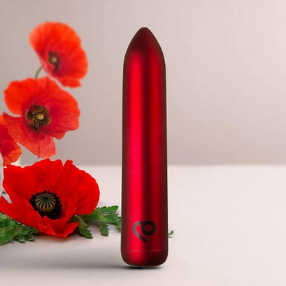 Red cylindrical bullet vibrator with a brand logo next to red flowers on a light background
