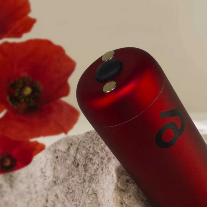 Red cylindrical object with a logo next to a red flower on a neutral background
