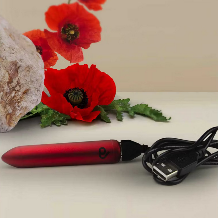 Red electronic massager with USB cable on a surface with red flowers in the background