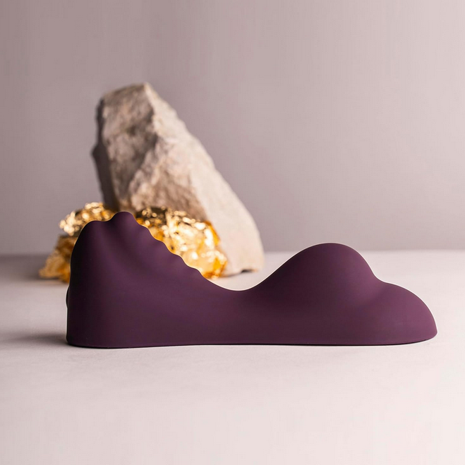 Purple wavy vibrator on a gray surface with a rock and crystals in the background